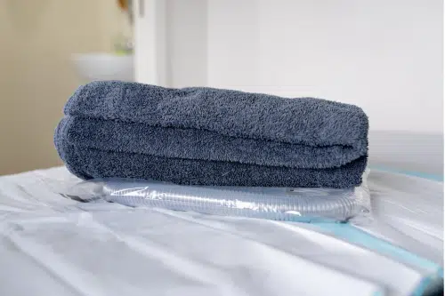 Fresh Towels and Equipment Prepared for Your Comfort Neatly folded dark grey towel placed on top of a packaged hose on a treatment bed in a clean clinical setting.